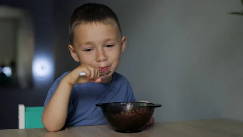 Cheerful child boy eats buckwheat porridge food as a dinner and smiling on Video stock 197798876