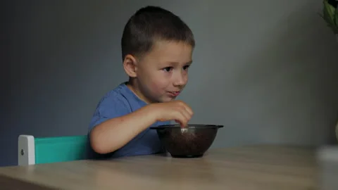 Cheerful child boy eats buckwheat porridge food as a dinner and smiling on Stock Footage 197799122