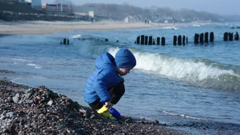 A cheerful child explores the sandy beach in a blue coat and bright yellow Stock Footage 314711180