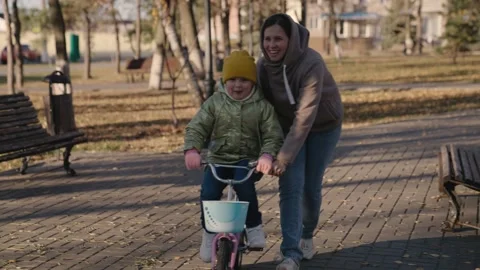 Cheerful child learns ride two-wheeled bike with his mother, happy family, kid Stock Footage 164568879