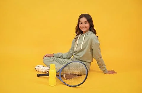 Cheerful child sit in sportswear with squash racket and water bottle on yellow Stock Photos