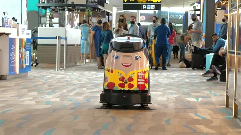 Cheerful cleaning robot navigates through busy airport terminal, Stock Footage 285773495