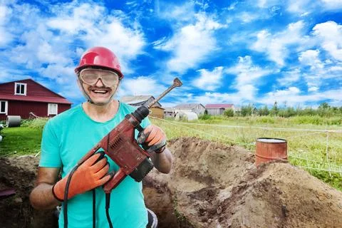 Cheerful construction worker with hammer drill in his hands. Stock Photos