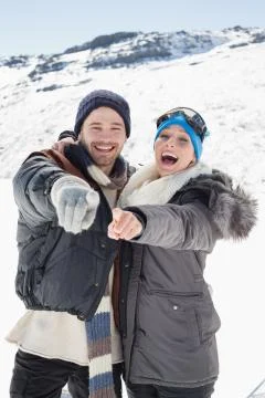 Cheerful couple in jackets pointing at camera on snow covered landscape Stock Photos