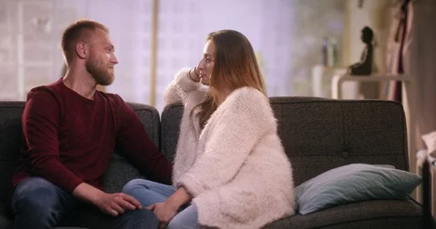 Cheerful couple sitting on couch talking and laughing Stock Footage 77394624