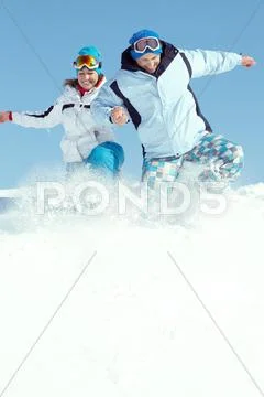 Cheerful couple in ski suit jumping in snow Stock Photos