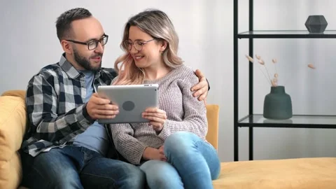 Cheerful couple smiling hugging use tablet together relaxing at home. 4k Dragon Video stock 148787147