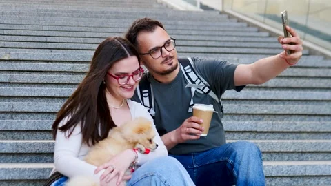 A Cheerful Couple Taking a Fun Selfie with Their Adorable Dog while Sitting on Stock Footage 307486019
