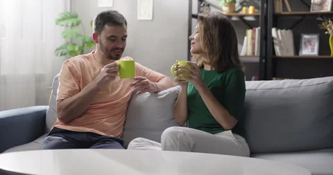 Cheerful couple talking drinking tea or coffee together in the living room Stock Footage 266925991
