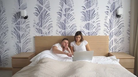 Cheerful couple using a computer lying on their bed at home Stock Footage 73993283