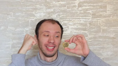 A cheerful, crazy, shaved and bearded guy with a bitcoin coin in his hands is Stock Footage 150709907