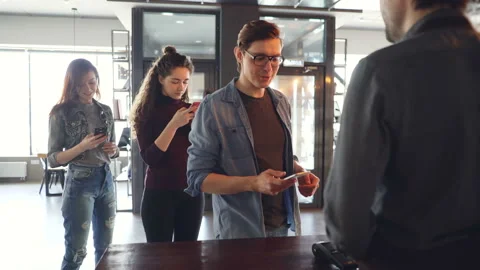 Cheerful customer in cafe is making payment with smartphone while queue of Stock Footage 89684189