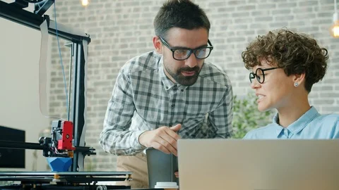 Cheerful developers talking producing model with 3d printer using laptop and Stock Footage 119766284
