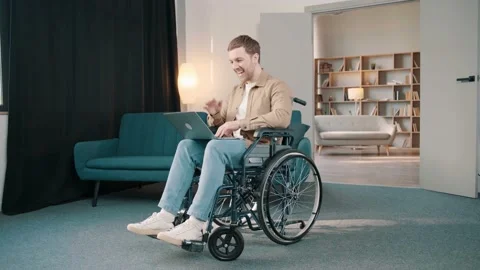 Cheerful disabled man on wheelchair using laptop in living room at home Stock Footage 236550569