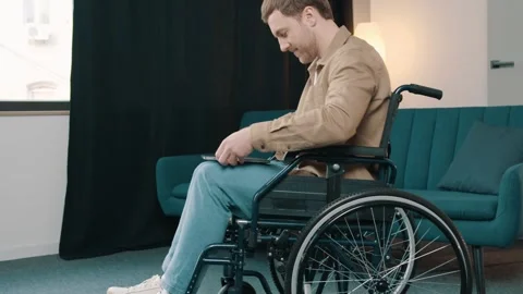 Cheerful disabled man on wheelchair using laptop in living room at home Video stock 244653537