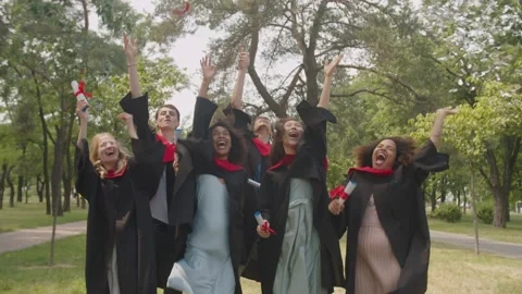 Cheerful diverse multiracial graduates celebrating graduation day, tossing up Stock Footage