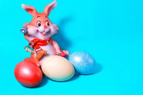 A cheerful Easter bunny on a blue background with colored eggs . Stock Photos