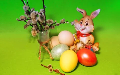 A cheerful Easter bunny on a green background with painted eggs and willow. Stock Photos