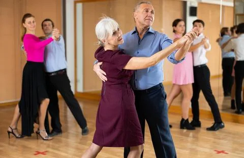 Cheerful elderly couple practicing ballroom dances in ballroom Stock Photos