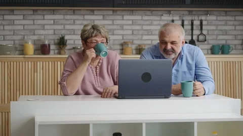 Cheerful elderly married pair is drinking tea at home kitchen and viewing movie Stock Footage 153395983