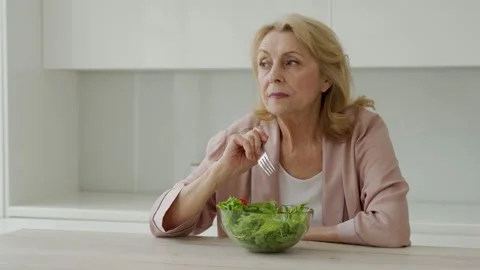 Cheerful elderly woman eats her vegetable salad and sits in the kitchen Stock Footage 161695848