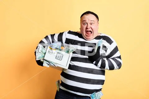 Cheerful fat criminal holding a safe full of money. robbery concept. Stock-Fotos