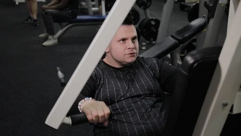 Cheerful fat man performs a wrong exercise in the gym. For the first time in a Stock Footage 105942524