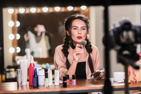 Cheerful female model applying makeup powder in dressing room Stock Photos