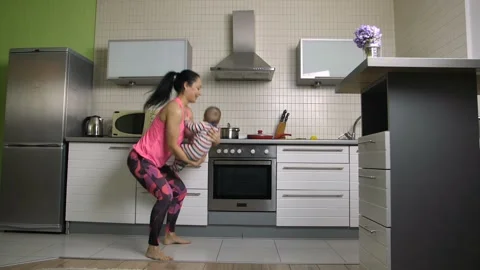 Cheerful fit mom doing squats with baby at home Video stock 85874679