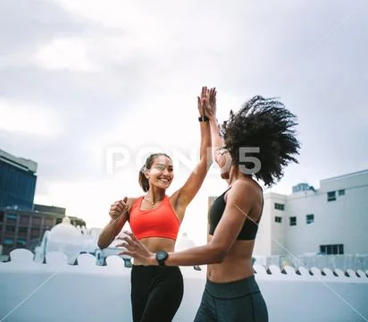 Cheerful fitness women giving high five while jogging on rooftop Stock Photos