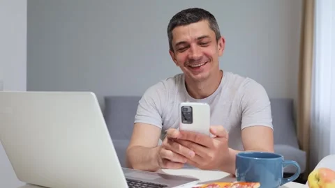 Cheerful friendly young man using mobile phone for video call while working on Stockbeeldmateriaal 292759309