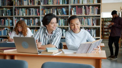 Cheerful girl and guy studying in university library talking using laptop books Stock Footage 116552425
