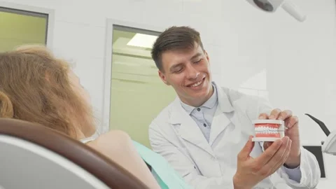 Cheerful girl beams at the camera while dentist showcases teeth model Stock Footage 311939070