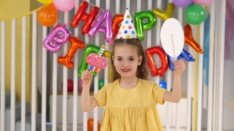 A cheerful girl with a festive hat and a pipe is having fun at a birthday party. Stock Footage 316589341