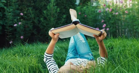 Cheerful girl reading book while lying on the back in the grass. Dolly shot Video stock 80070947