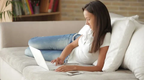 Cheerful girl relaxing on sofa using laptop looking at camera and smiling Stock Footage 34197036