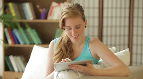 Cheerful girl sitting on sofa using touchpad looking at camera and smiling Stock Footage 34831379