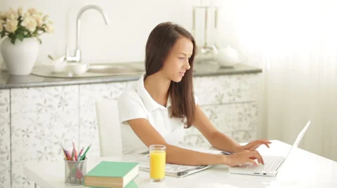 Cheerful girl sitting at table using laptop drinking juice looking at camera  Видео 34196028