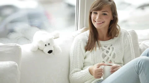 Cheerful girl sitting by window drinking tea looking at camera and smiling Stock Footage 34150164