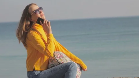 Cheerful girl in yellow golf speaks on phone against sea Stock Footage