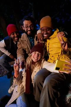 Cheerful group of multiethnic friends using phone to take a selfie while Stock Photos