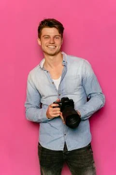 Cheerful guy with camera on pink background. Stock Photos