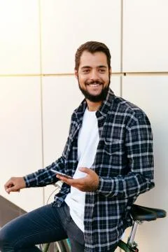 Cheerful guy holds a smartphone while sitting on bike Stock Photos