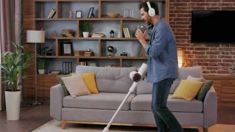 Cheerful guy, the man cleans the apartment. Vacuuming, wearing headphones with Video stock 208786909