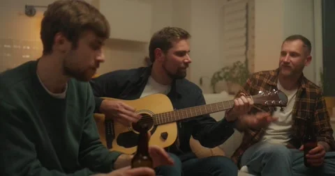 A cheerful guy plays the guitar while his friends sing and plays along with him Stock Footage 313265220