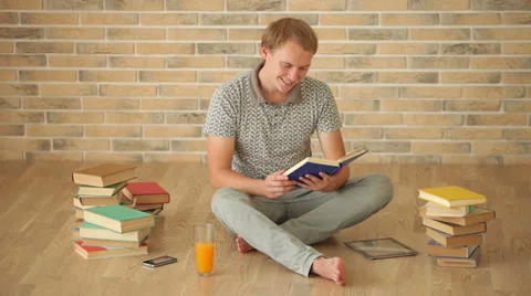 Cheerful guy sitting on floor reading book looking at camera and smiling Stock Footage 34278136