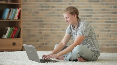 Cheerful guy sitting on floor using laptop closing it looking at camera  Stock Footage 34278150