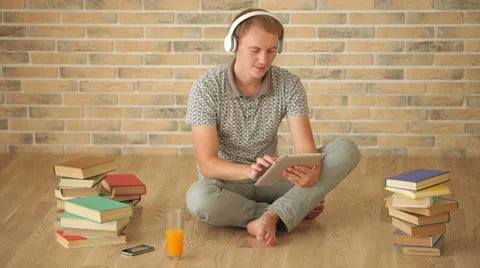 Cheerful guy sitting on floor using touchpad drinking juice looking at camera Video stock 34278169