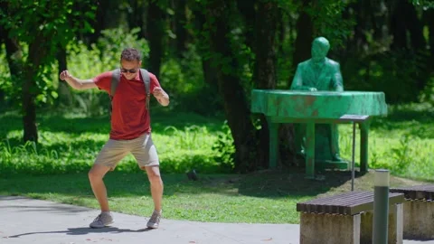 Cheerful guy in sunglasses and backpack cheerfully rejoicing and dancing in park Vídeo Stock 246879957