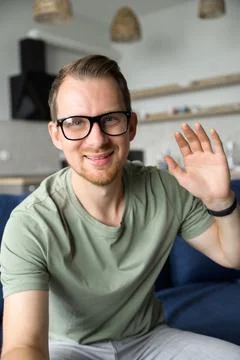 A cheerful guy is waving hello into webcam, smiles and greeting Stock Photos